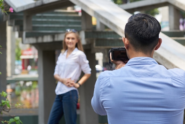 笑顔のガールフレンドの写真を撮るデジタルカメラを持つ若い男