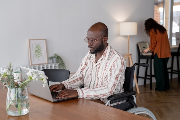 Young man with disability in casual shirt networking in front of laptop