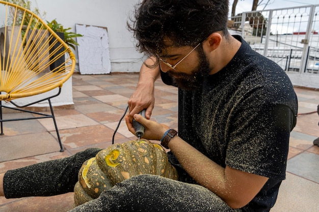 Young man with a drill or dremel drilling a pumpkin for halloween