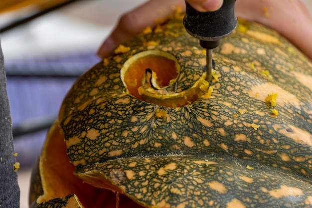 Young man with a drill or dremel drilling a pumpkin for halloween