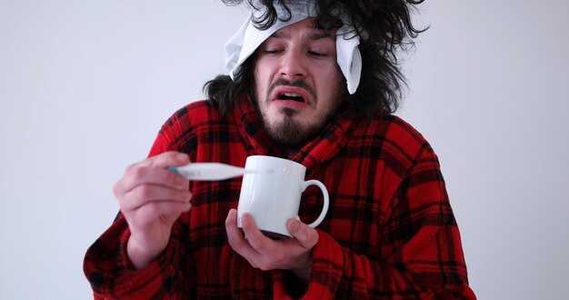 インフルエンザと熱を持つ若い男は、白で隔離された癒しのお茶のカップを保持しています