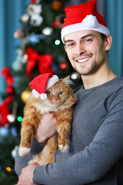 Young man with fluffy red cat near the Christmas tree