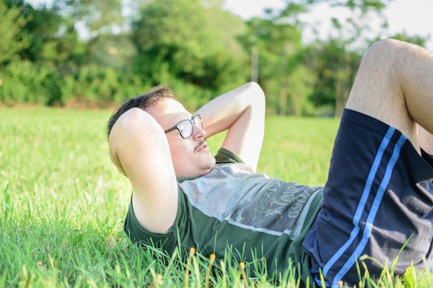 写真 メガネと緑の t シャツを着た若い男が腹筋をし、公園で運動する