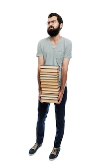 Un giovane con gli occhiali e la barba tiene tra le mani una grossa pila di libri. istruzione e formazione. isolato. verticale. a tutta altezza.
