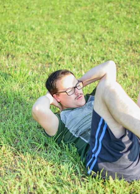 Young man with glasses and green tshirt doing situps and exercising in park