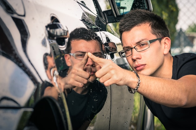 Giovane uomo con gli occhiali ispezione auto di lusso al commercio di seconda mano