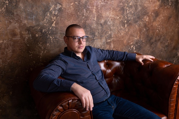 young man with glasses sits in a leather chair