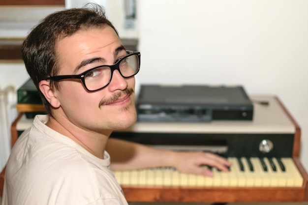 Young man with glasses and white tshirt looking at camera with his piano