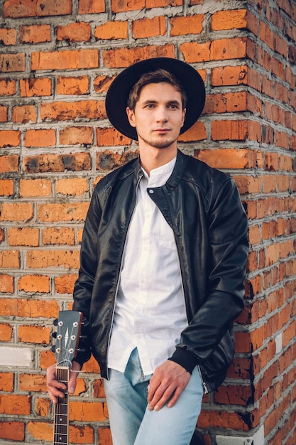 レンガの壁の背景にギターを持つ若い男