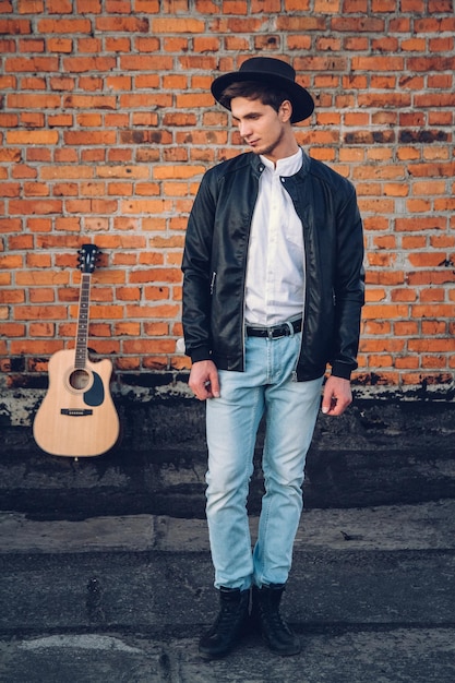 Young man with a guitar on the background of a brick wall