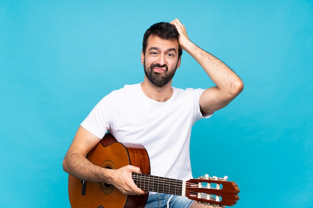 Young man with guitar over isolated blue with an expression of frustration and not understanding