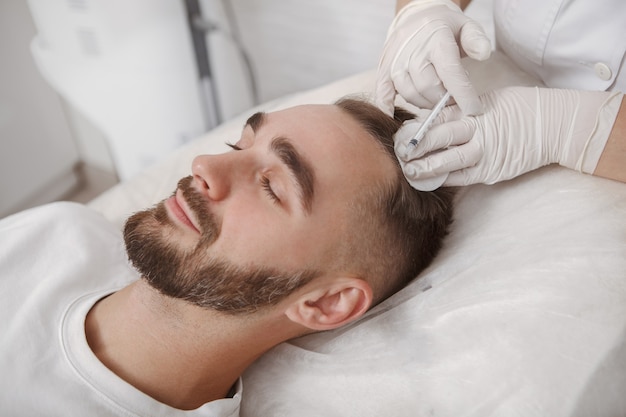 Young man with hairloss problem receiving injections in scalp by trichology doctor