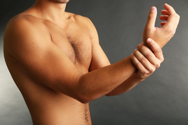 Young man with hand pain on grey background