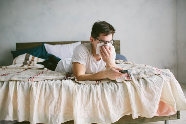 Young man with handkerchief. Sick guy on the bed has runny nose. man makes a cure for the common cold.