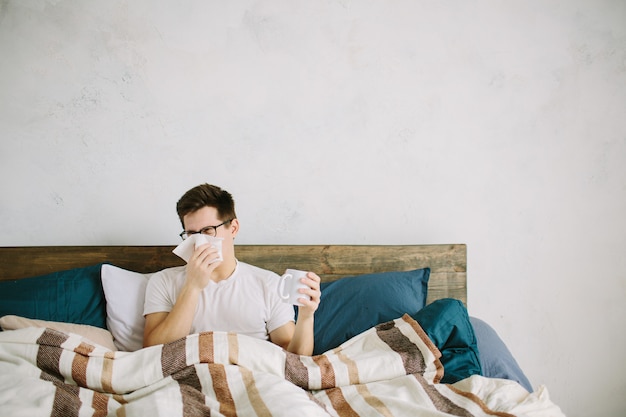 Young man with handkerchief. Sick guy on the bed has runny nose. man makes a cure for the common cold