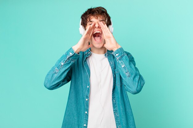 Young man with headphones feeling happy,giving a big shout out with hands next to mouth