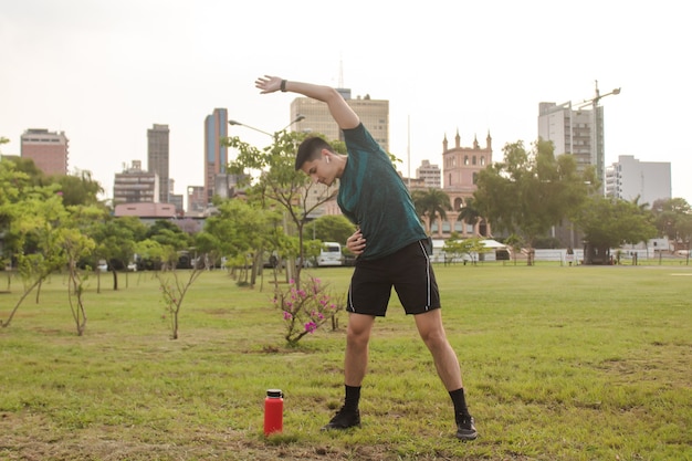 Young man with headphones stretching in the park.