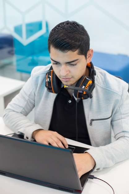 Young man with headphones, working on the computer in coworking office.