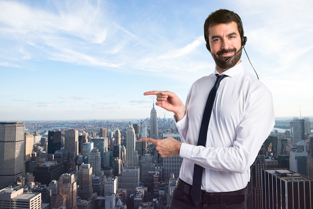 Young man with a headset pointing to the lateral on unfocused background