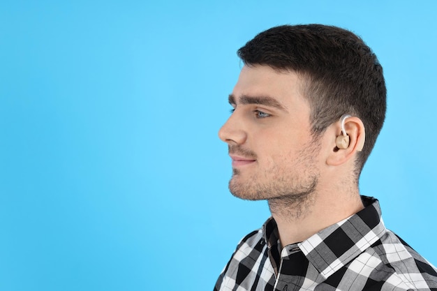 Young man with hearing aid on blue background