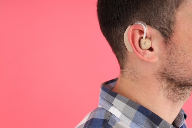 Young man with hearing aid on pink background