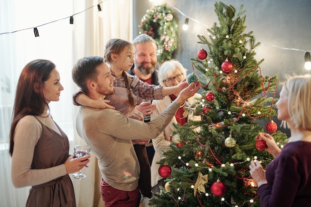 Giovane con la sua piccola figlia e altri membri della famiglia in piedi vicino all'albero di natale a casa mentre si prepara per le vacanze