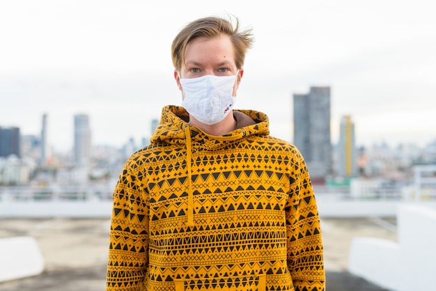 Young man with hoodie wearing mask for protection from corona virus outbreak against view of the city