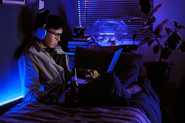 Young man with huge headphones on head holding bottle of beer and scrolling social media while