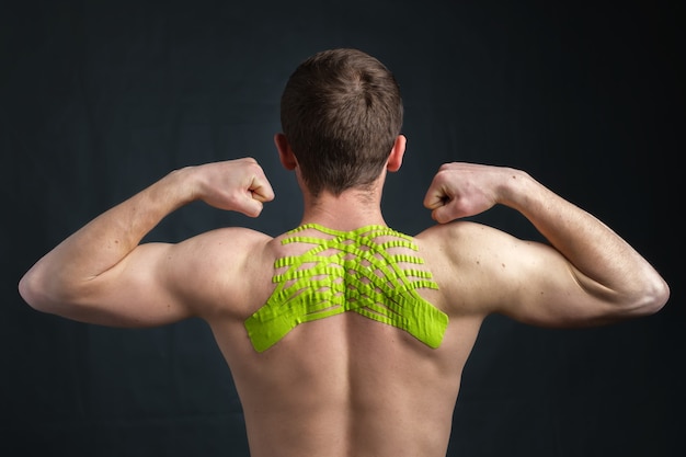 Young man with kinesiology medical tape on his neck showing biceps