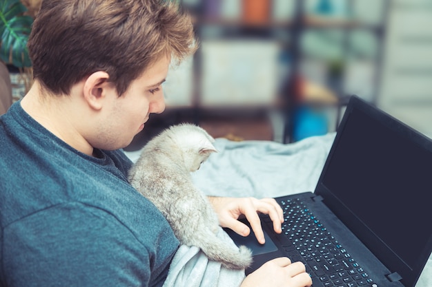 Young man with kitten working at his laptop. The concept of online learning and work.