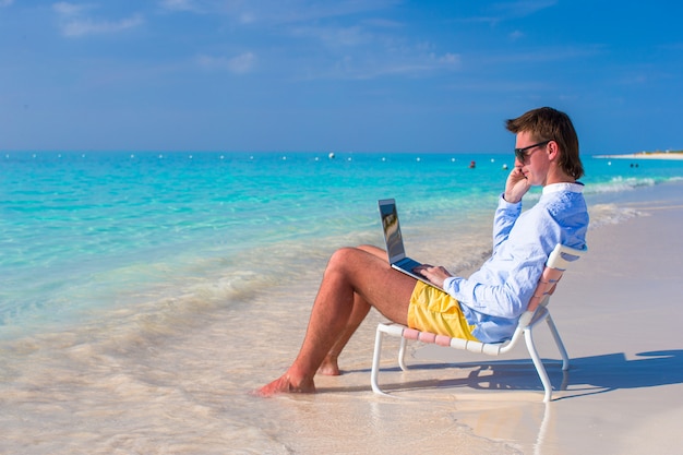 Young man with laptop and cell phone on tropical beach