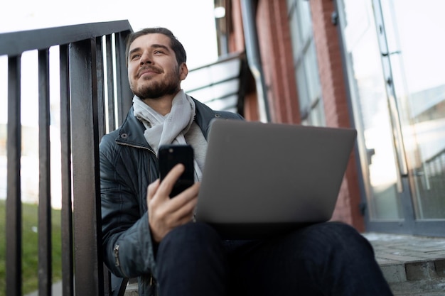 Young man with laptop on his lap outside taking training courses