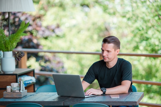 Young man with laptop in outdoor cafe drinking coffee. Man using mobile smartphone.