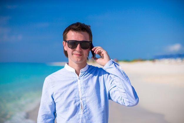 Young man with laptop and phone on the background of turquoise ocean at tropical beach