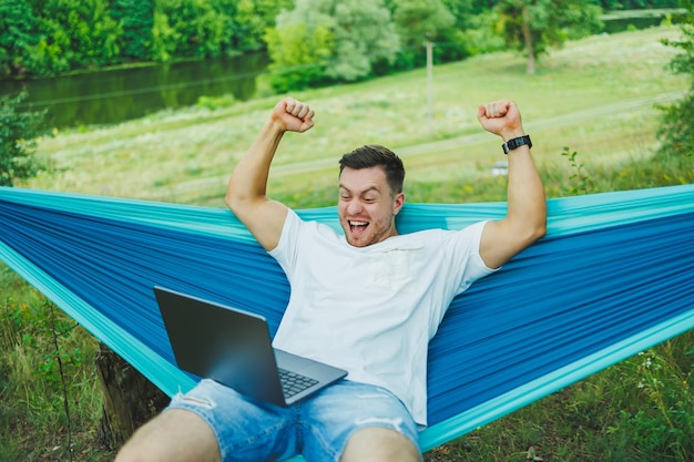 A young man with a laptop sits in a hammock in nature and works remotely Work in nature during vacation