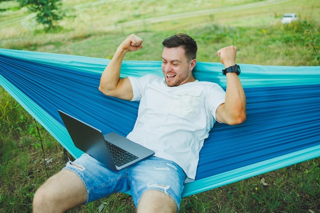 A young man with a laptop sits in a hammock in nature and works remotely Work in nature during vacation