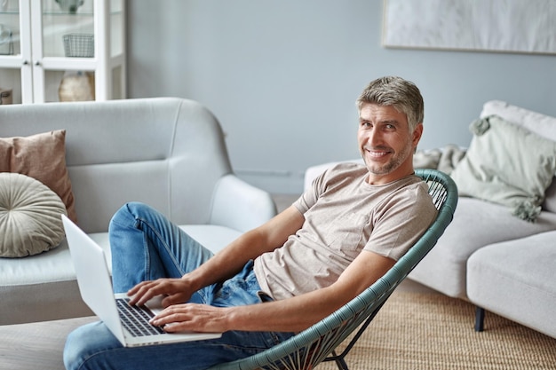 Young man with a laptop sitting in a cozy armchair