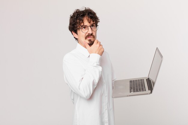 Young man with a laptop thinking, feeling doubtful and confused