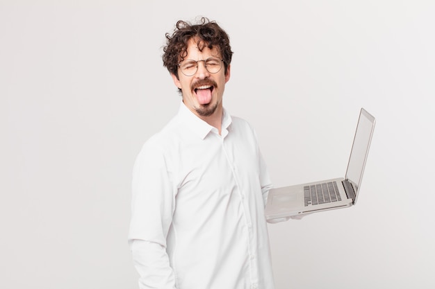 Young man with a laptop with cheerful and rebellious attitude, joking and sticking tongue out