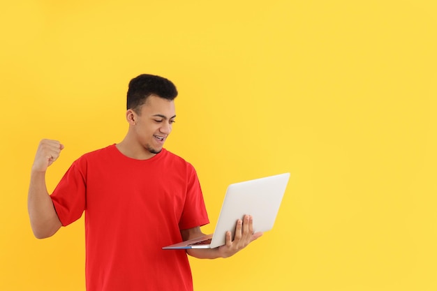 Young man with laptop on yellow background