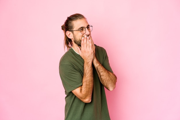 Young man with long hair look laughing about something, covering mouth with hands.