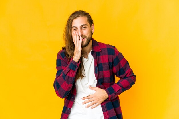 Young man with long hair look laughs happily and has fun keeping hands on stomach