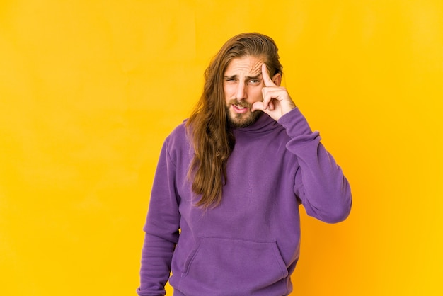 Young man with long hair look pointing temple with finger, thinking, focused on a task.