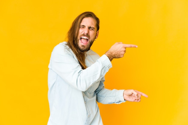 Young man with long hair look pointing with forefingers to a copy space, expressing excitement and desire.