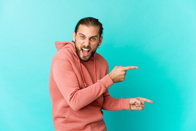長い髪の若い男は、人差し指でコピースペースを指差して、興奮と欲望を表現しています。