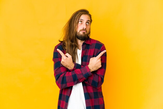 Young man with long hair look points sideways, is trying to choose between two options.