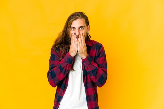 Young man with long hair look shocked, covering mouth with hands