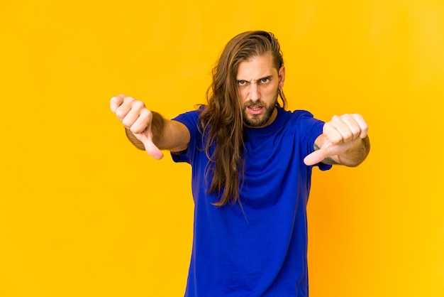 Young man with long hair look showing thumb down and expressing dislike.