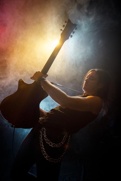 Young man with long hair with electric guitar in neon lights Rock musician plays in atmosphere of stage