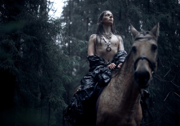 Giovane con capelli lunghi con cavallo nella foresta oscura.